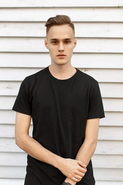 Hombre guapo en camiseta negra cerca de la pared de madera blanca . — Foto de Stock