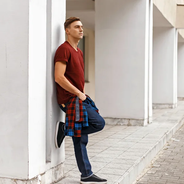 Tişört ve kot pantolonla spor ayakkabı beyaz duvara yakın duran yakışıklı adam.