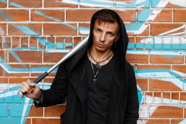 Angry guy near brick wall with graffiti holding a metal bat