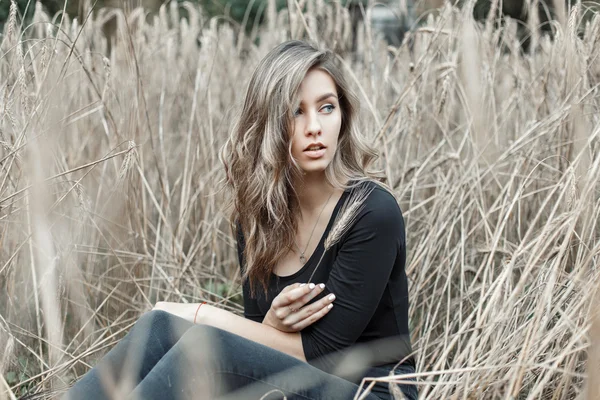 Kuru otların arasında oturan güzel genç kadın. Buğday alanı