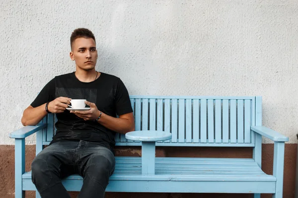 Красивий молодий чоловік з кавою на лавці — стокове фото