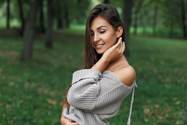 Schöne, glückliche junge Frau lächelt in einem grauen Pullover in einem grünen Park. — Stockfoto