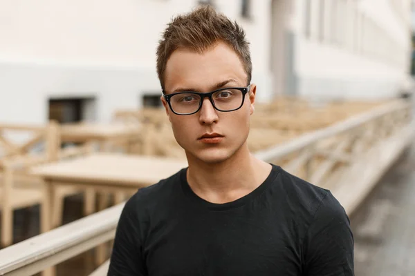 Handsome young man with glasses in a black shirt standing on the street. — Stock Photo, Image