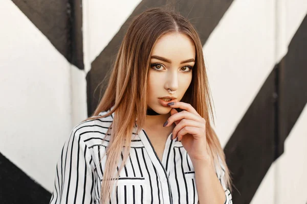 Beautiful model woman with an earring in the nose in fashionable clothes posing near the wall. Black and white stripes. — Stock Photo, Image