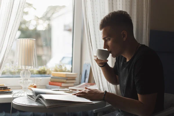 Молодий чоловік відпочиває в ресторані, читає книгу і п'є каву . — стокове фото