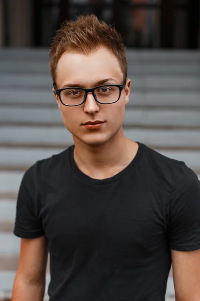Hermoso joven con estilo en una camisa negra y gafas hipster — Foto de Stock