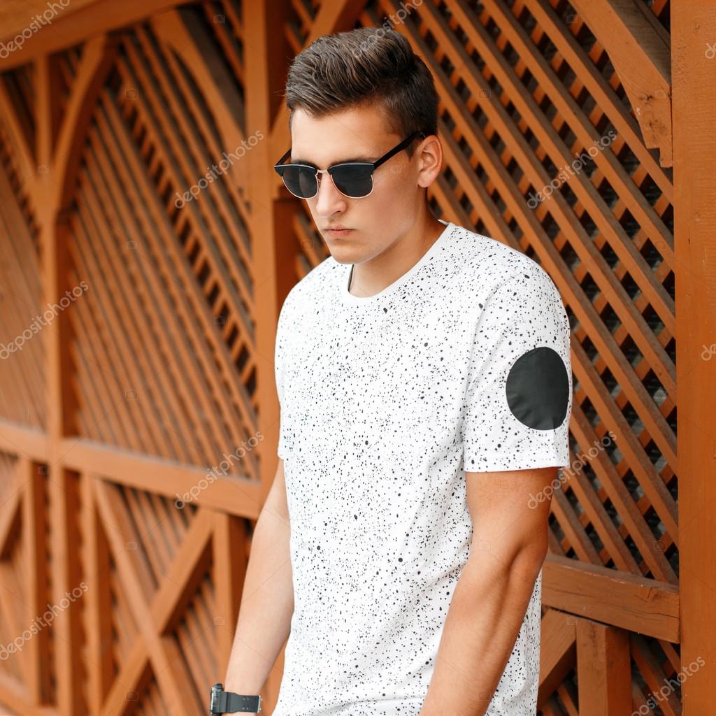 Handsome young man with sunglasses and hairstyle standing near the wooden wall