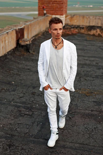 Beyaz bir ceket, beyaz kot ve beyaz spor ayakkabı çatıda yürürken saçlı yakışıklı genç adam