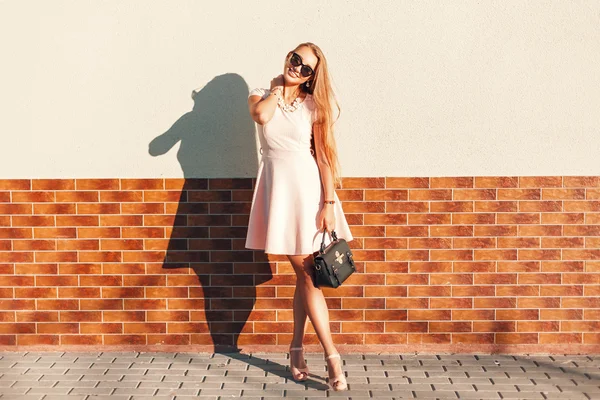 Красивая женщина в розовом платье с сумочкой в солнечный день стоит у стены — стоковое фото