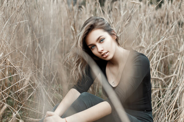 Beautiful young girl in a black T-shirt sitting in the dry grass.