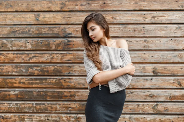 Bella ragazza elegante in un maglione e una gonna vicino alla parete di legno — Foto Stock