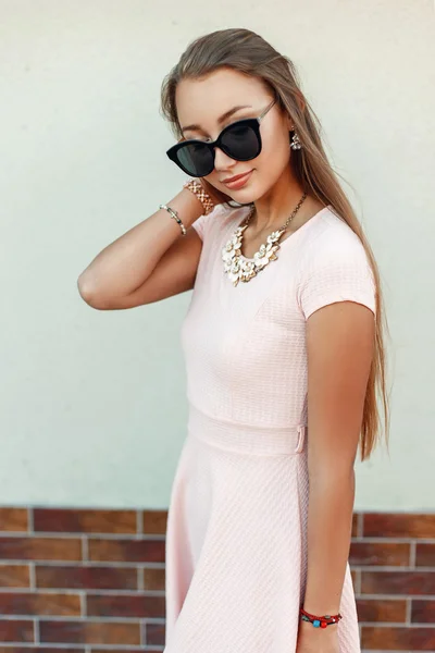 Ładna kobieta z okulary przeciwsłoneczne w różowej sukni w pobliżu zielonej ścianie — Zdjęcie stockowe