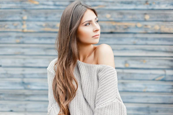 Mooie jonge vrouw met het kapsel in een vintage grijze trui in de buurt van de blauwe muur — Stockfoto