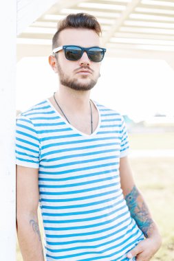 Güneşli bir günde sahilde duran güneş gözlüğü sakallı yakışıklı hipster adam.