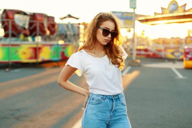 Güzel kadın güneş gözlüğü ve günbatımı parkta beyaz bir T-shirt.