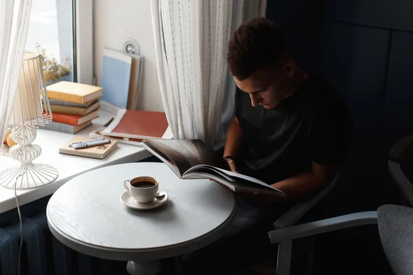 Hermoso hombre moderno descansar en un restaurante, leer un libro y beber café . — Foto de Stock