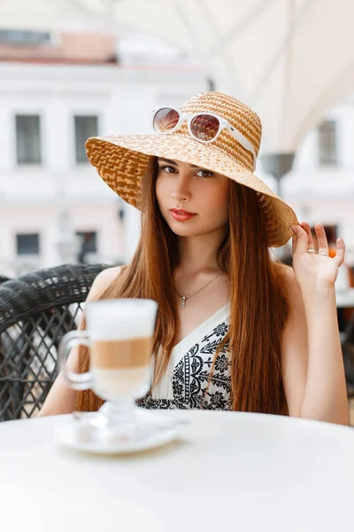 Hermosa mujer en un sombrero de paja y gafas de sol descansando en un café de verano y beber café . — Foto de Stock