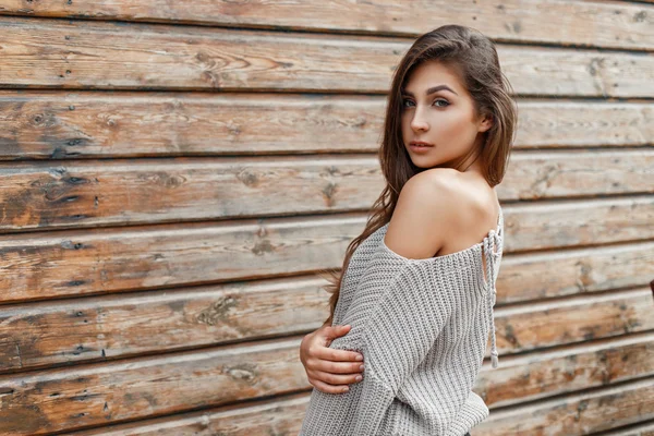 Sexy schöne Frau in einem grauen Pullover steht in der Nähe der Holzwand — Stockfoto