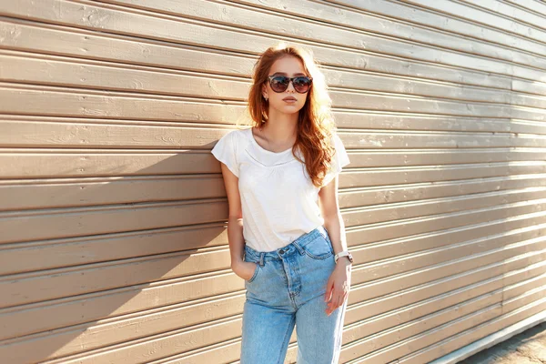 Belle fille élégante dans un jean bleu vintage et T-shirt blanc debout près d'un mur en bois . — Photo