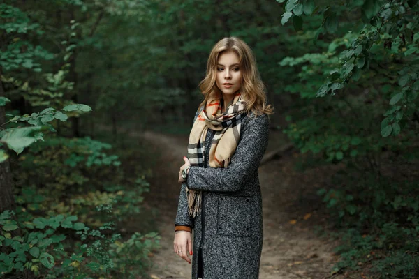 Piękna młoda kobieta w dziany szalik i Jesienny płaszcz w pobliżu zielonych liści — Zdjęcie stockowe