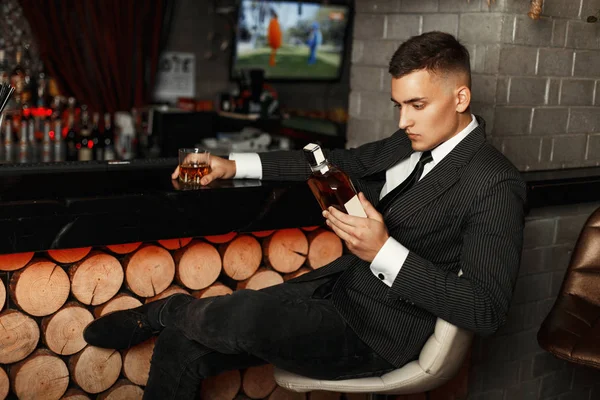 Joven guapo con un elegante traje sosteniendo una botella de whisky en el bar . — Foto de Stock