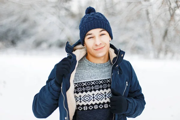 Fiatal jóképű férfi mosolyogva a téli ruházat, a kötött pulóvert, pózol a park mintával. — Stock Fotó