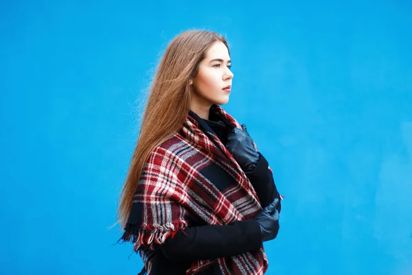 Female profile. Beautiful young girl with a scarf and coat near the blue wall