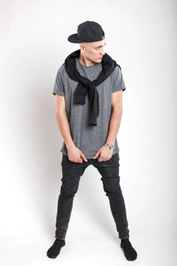 Beysbol şapkası bir gri gömlek ve stüdyoda beyaz bir arka plan üzerinde siyah kot ile yakışıklı genç adam