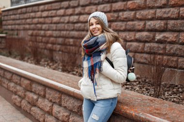 Neşeli güzel kız beyaz ceket ve eşarp bir tuğla duvar yakınındaki bir gülümseme