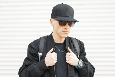 Güneş gözlüğü ve siyah beysbol şapkası beyaz bir duvar yakınındaki şık yakışıklı