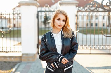 Güzel sarışın kadın moda siyah ceket ve güneşli bir çit yakınındaki beyaz polo gömlek