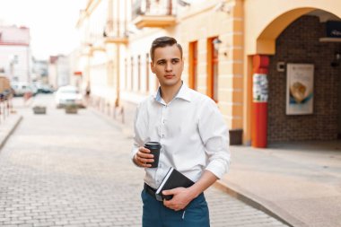 Genç yakışıklı olan kahve ve bir dizüstü bilgisayar ile şehirde yürür