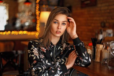 Çiçekli siyah ceketli güzel kadın bir kafede oturuyor