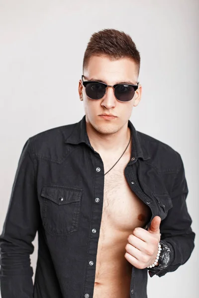 Homme sexy en lunettes de soleil et une chemise noire posant en studio sur un fond blanc — Photo