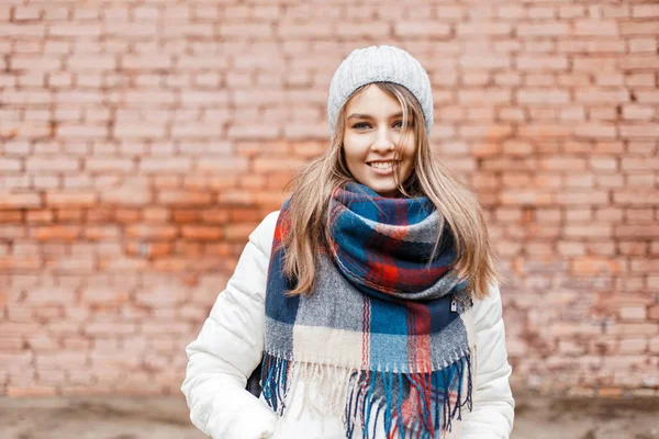 Красива стильна дівчина з білою посмішкою в теплій куртці і яскравим шарфом біля цегляної стіни — стокове фото