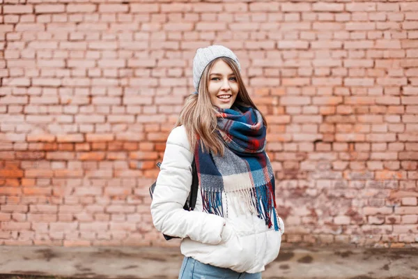 Jovem mulher sorrindo em uma jaqueta branca e cachecol elegante brilhante perto da parede — Fotografia de Stock
