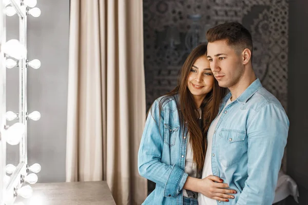 Jonge gelukkige paar met een glimlach in jeans kleding in de buurt van een vintage spiegel met verlichting — Stockfoto