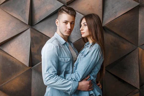 Hermosa pareja en ropa de mezclilla de moda abrazándose cerca de una pared de madera — Foto de Stock