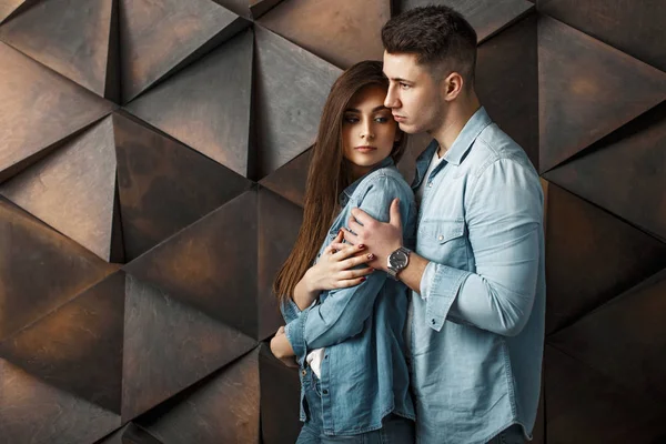 Tineri cuplu frumos în haine de denim la modă stau lângă peretele modern din lemn — Fotografie, imagine de stoc