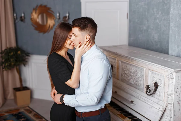 Jonge knappe man met een gelukkig vriendin in elegante kleren knuffelen in de buurt van een vintage piano — Stockfoto