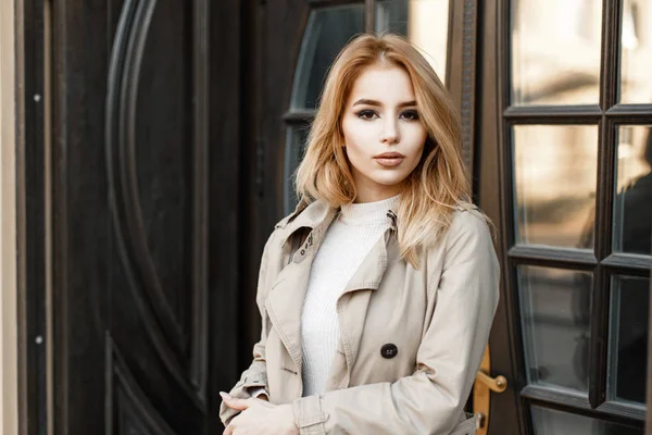 Beautiful young woman in a trendy coat near a vintage wooden door — Stock Photo, Image