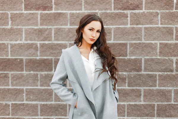 Beautiful woman in a fashionable gray coat near the wall — Stock Photo, Image