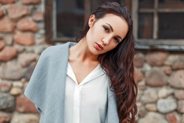 Retrato de uma bela mulher elegante em um casaco cinza e blusa branca contra um fundo de uma parede de pedra — Fotografia de Stock