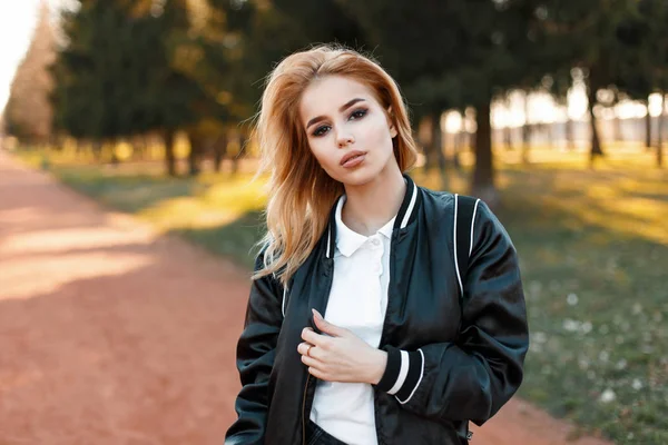 Mulher loira bonita em um casaco preto e uma camisa de pólo branco em um parque em um dia ensolarado — Fotografia de Stock