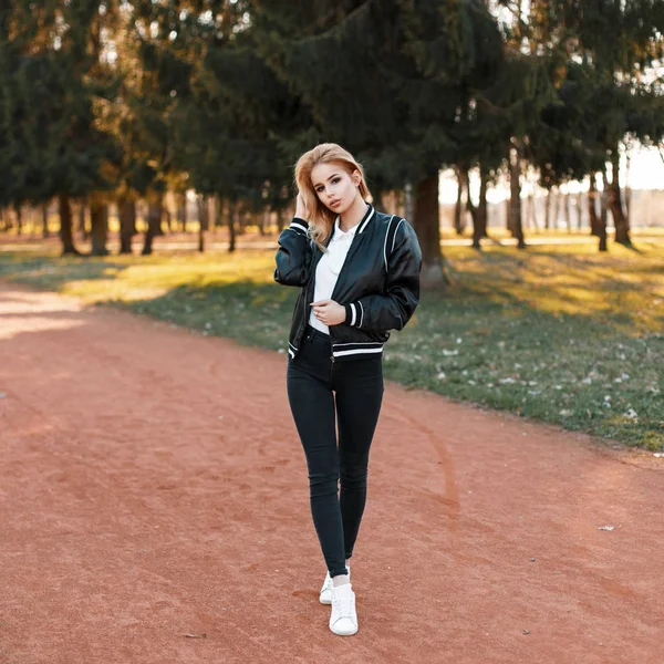 Красивая женщина в черной куртке, черных джинсах и белых туфлях в парке в солнечный день — стоковое фото