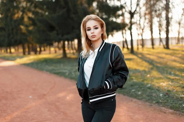 Модна молода блондинка в чорній куртці і біле поло прогулянки в парку — стокове фото