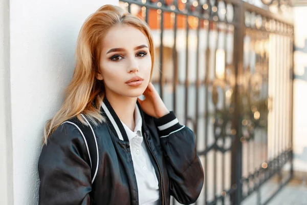 Belle femme blonde en vêtements à la mode près d'un mur blanc d'une clôture — Photo