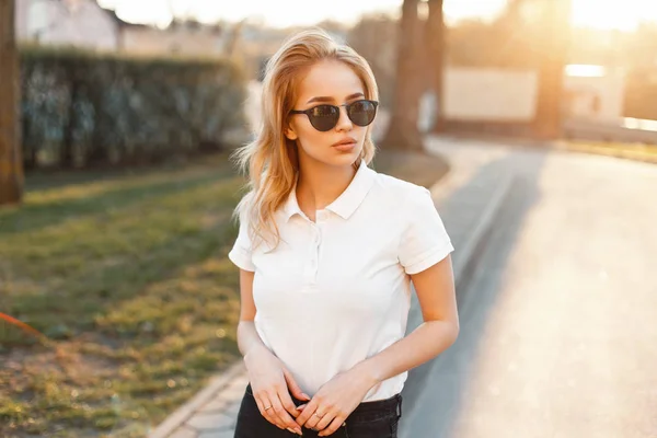 Menina em óculos de sol na moda e camisa de pólo branco em um dia de primavera ao pôr do sol — Fotografia de Stock