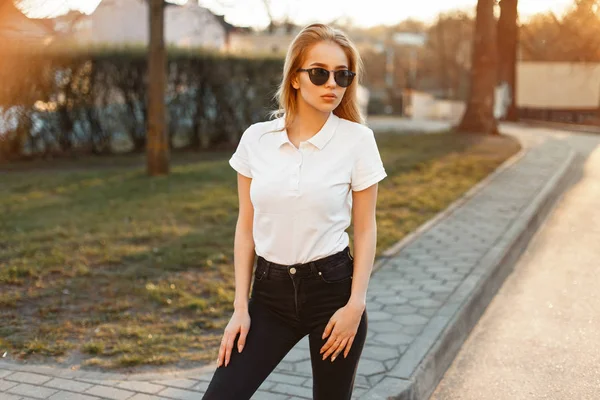 Женщина в солнечных очках в белой рубашке в черных джинсах на закате — стоковое фото