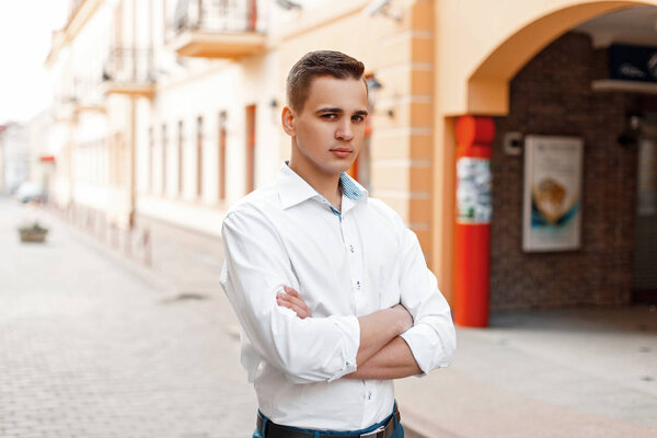 Portrait of a man with a crossed hand in a white shirt on the street
